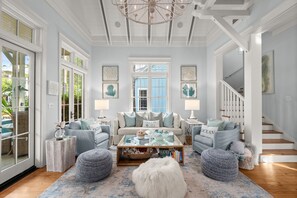 A spacious living room with a large window, a chandelier, and a staircase.