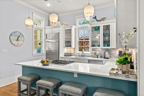 A modern kitchen with a large island, bar stools, pendant lights, and a clock on the wall.