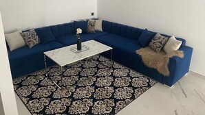 Una sala de estar moderna con un sofá modular azul, una mesa de centro blanca, un tapete estampado y un reloj de pared.