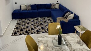 Una sala moderna con un sofá modular azul, un tapete estampado, una mesa de comedor con cubierta de mármol y un reloj de pared.
