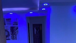 Un couloir éclairé d’une lumière bleue, une porte au fond et une chaise sur la droite.