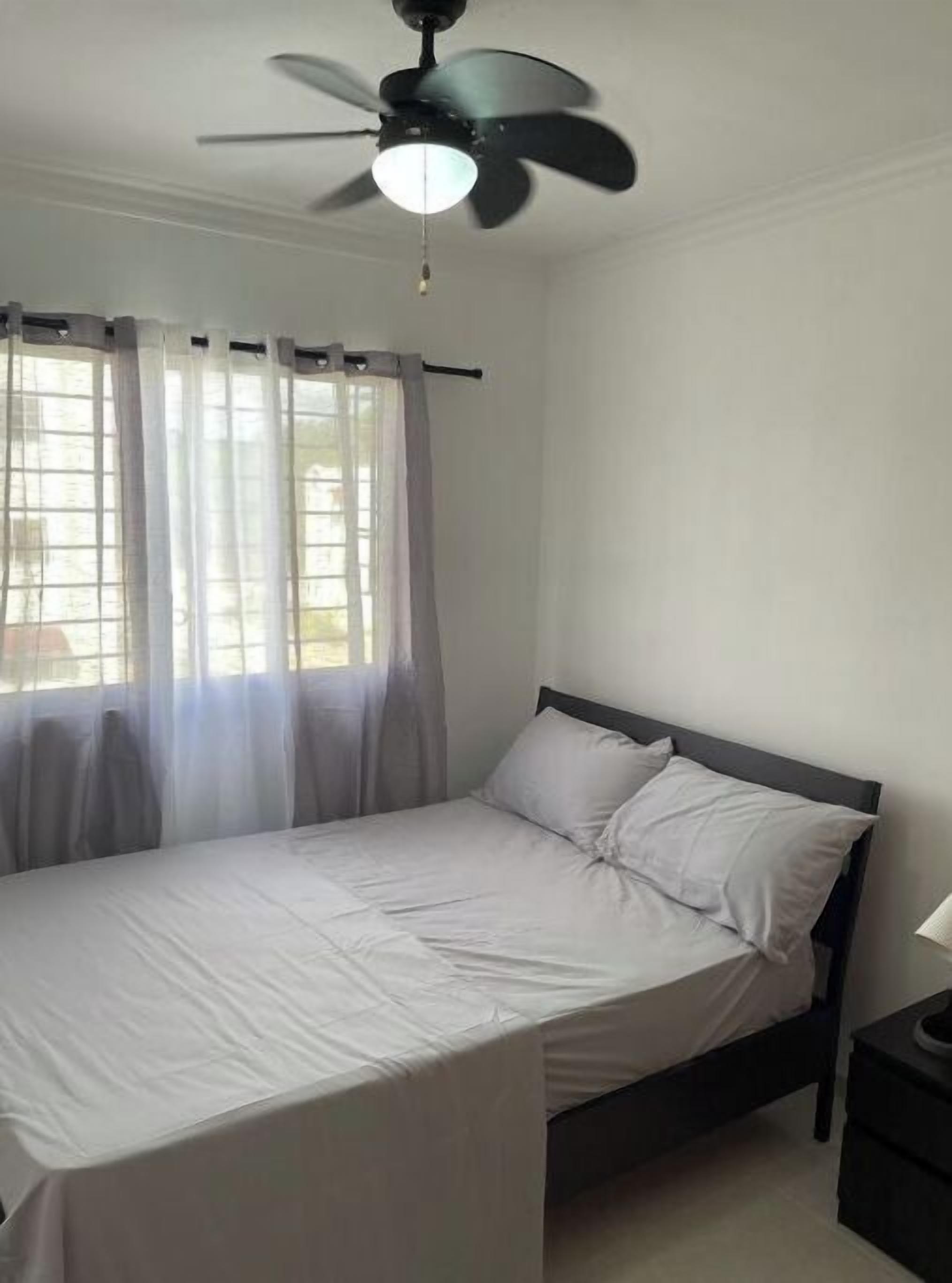 Un dormitorio con cama, ventilador de techo y ventana con cortinas de encaje.