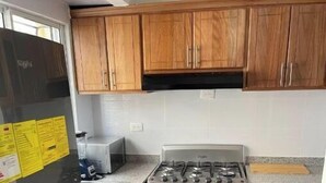Une cuisine de taille réduite, dotée de meubles en bois, d’un réfrigérateur en acier inoxydable et d’une cuisinière à gaz.
