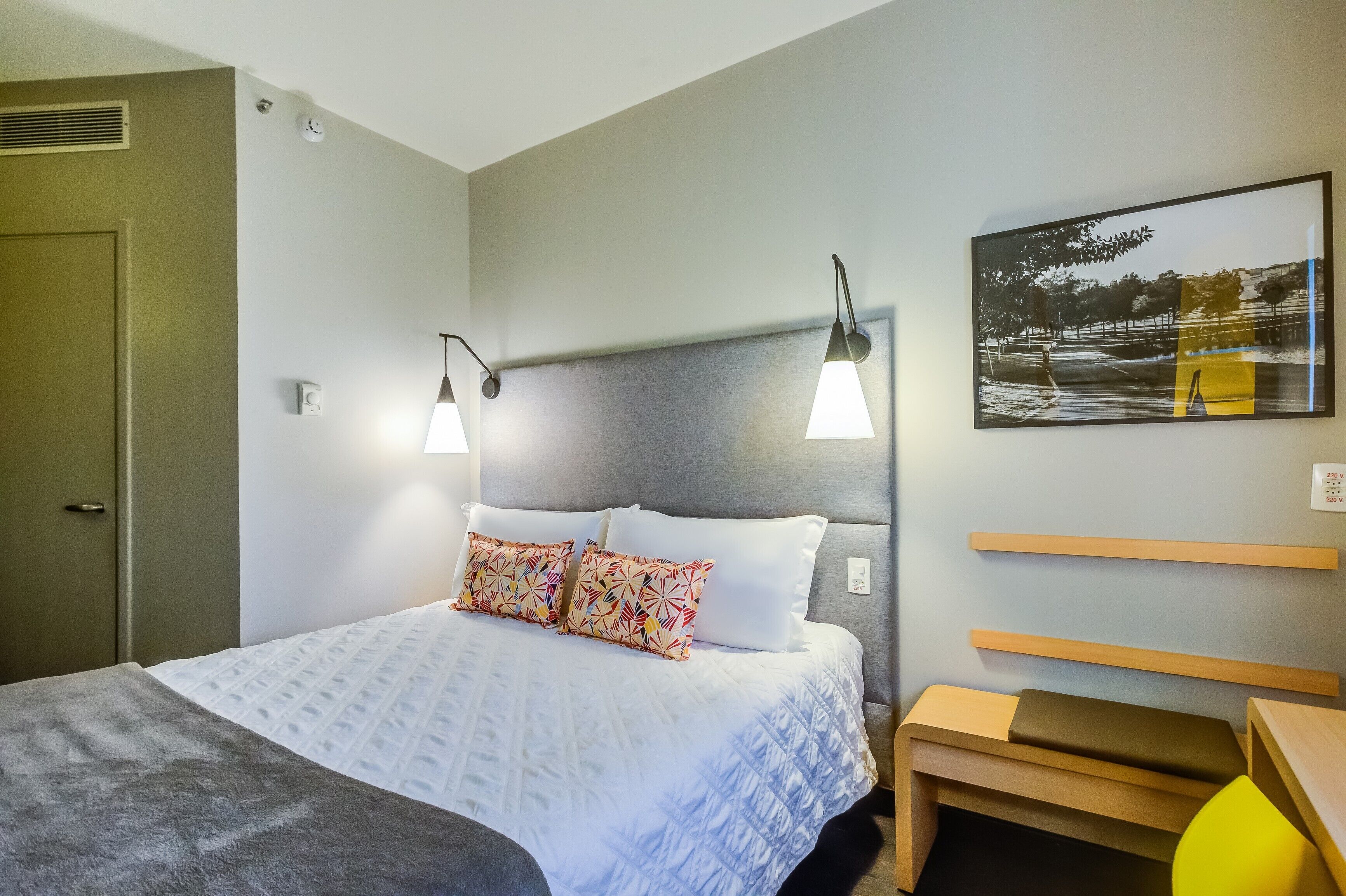 A neatly arranged hotel room with a bed, bedside lamps, a bedside table, and a wall-mounted shelf.
