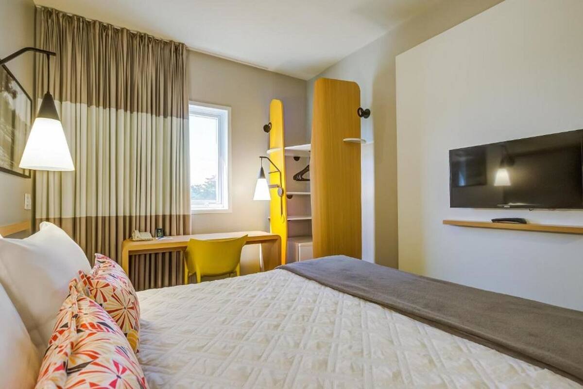 Une chambre d’hôtel équipée d’un lit, d’un bureau, d’une chaise, d’une télévision et d’une fenêtre avec des rideaux.