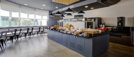 A modern kitchen area with a central island, black pendant lights, and a large window providing natural light.
