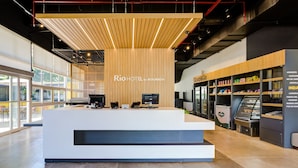 Ein moderner Hotel-Empfangsbereich mit einer gut sichtbaren Rezeption, einem digitalen Bildschirm und einem Gr&Go Self-Service-Terminal.