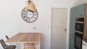 A modern kitchen with a wooden dining table, two wicker chairs, a large wall clock, and built-in appliances. - 4 Bedroom Private vacation home in Baden (Baden)