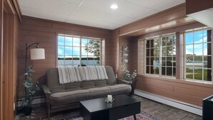 A cozy living room with a brown sofa, a coffee table, and a large window offering a view of a lake.