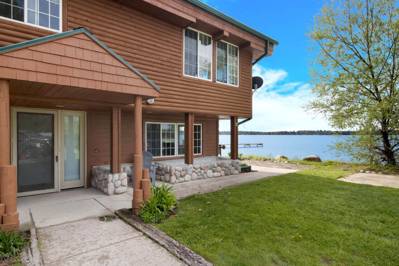 A two-story house with a covered porch, stone foundation, and a view of a lake.