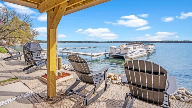 An outdoor seating area with Adirondack chairs, a grill, and a view of a lake with boats.