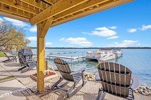 Un espace extérieur aménagé avec des chaises Adirondack, un barbecue et une vue sur un lac où l’on peut voir des bateaux.