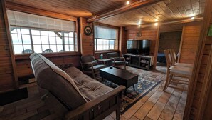 A cozy cabin-style room with a sofa, chairs, a TV, and a fireplace.