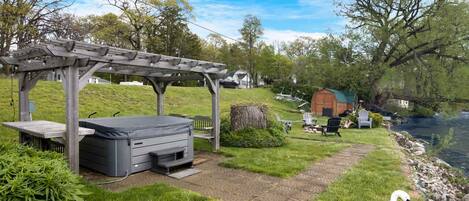 A gazebo with a hot tub, a grassy path, a swan, and a river.