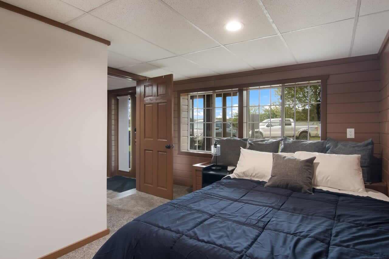 Un dormitorio con una cama grande, una mesita de noche, una lámpara y una ventana con vistas a coches aparcados afuera.