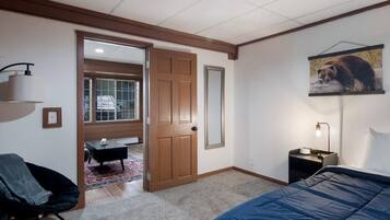 Un dormitorio con cama, una silla, una mesita de noche, una puerta y un cuadro colgado en la pared.