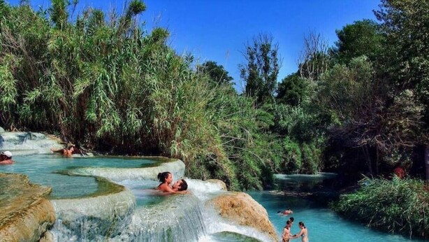 A natural hot spring with clear water surrounded by lush greenery.