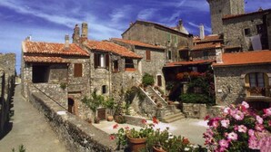 A historic stone building with a tower, terracotta roof tiles, and a narrow street with steps leading to the entrance.