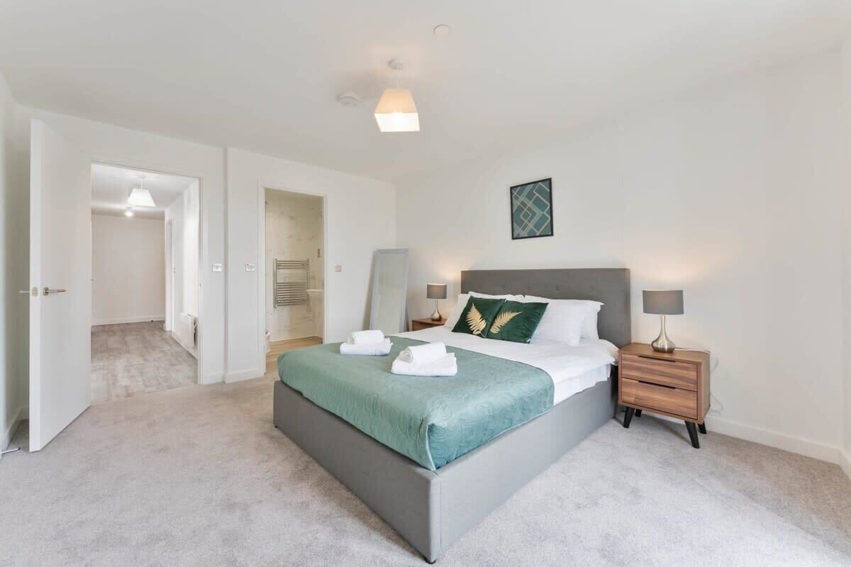 A modern bedroom with a large bed, bedside tables, a nightstand, and a wall-mounted lamp.