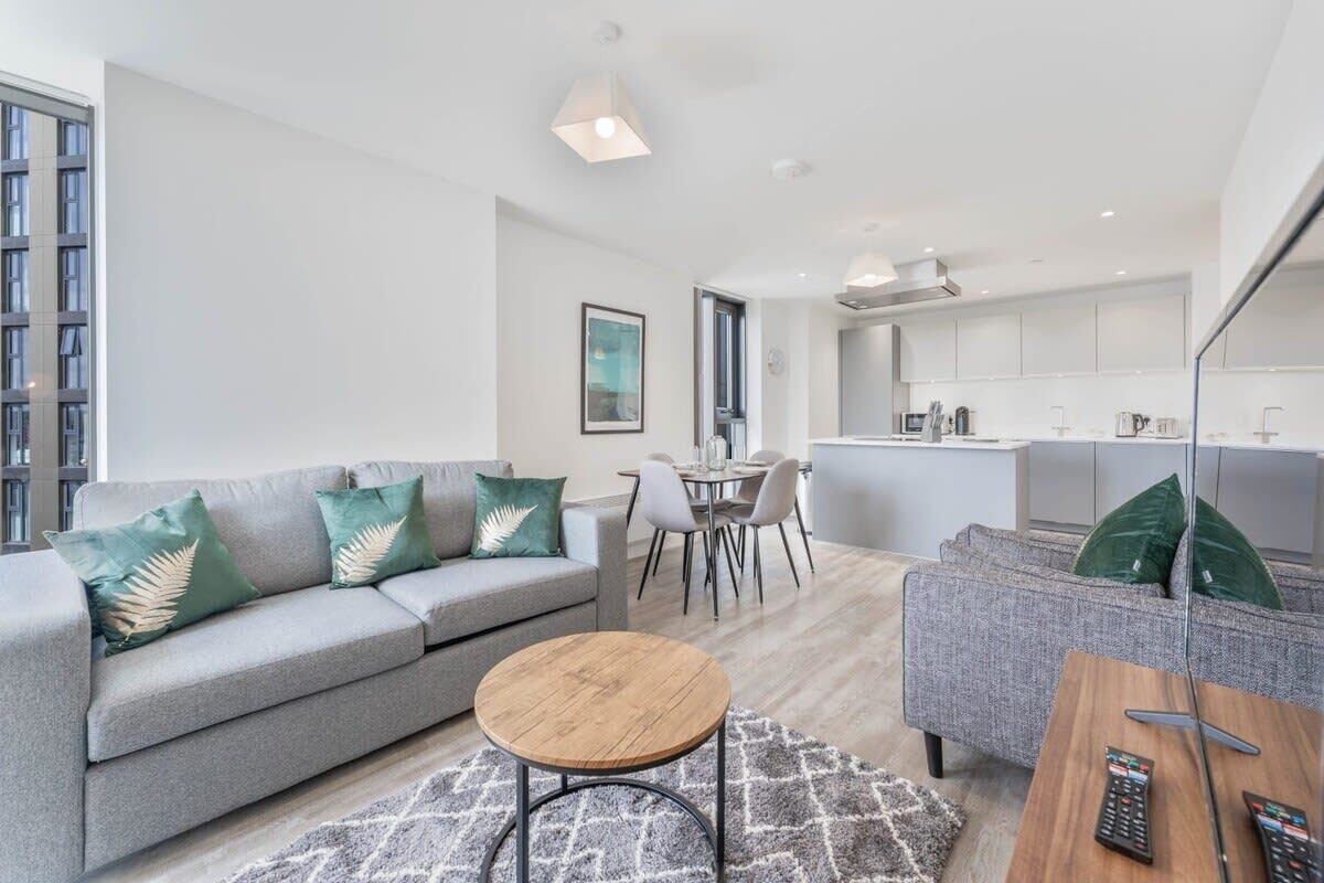 A modern apartment with a grey sofa, a round wooden coffee table, and a dining area with a white table and chairs.