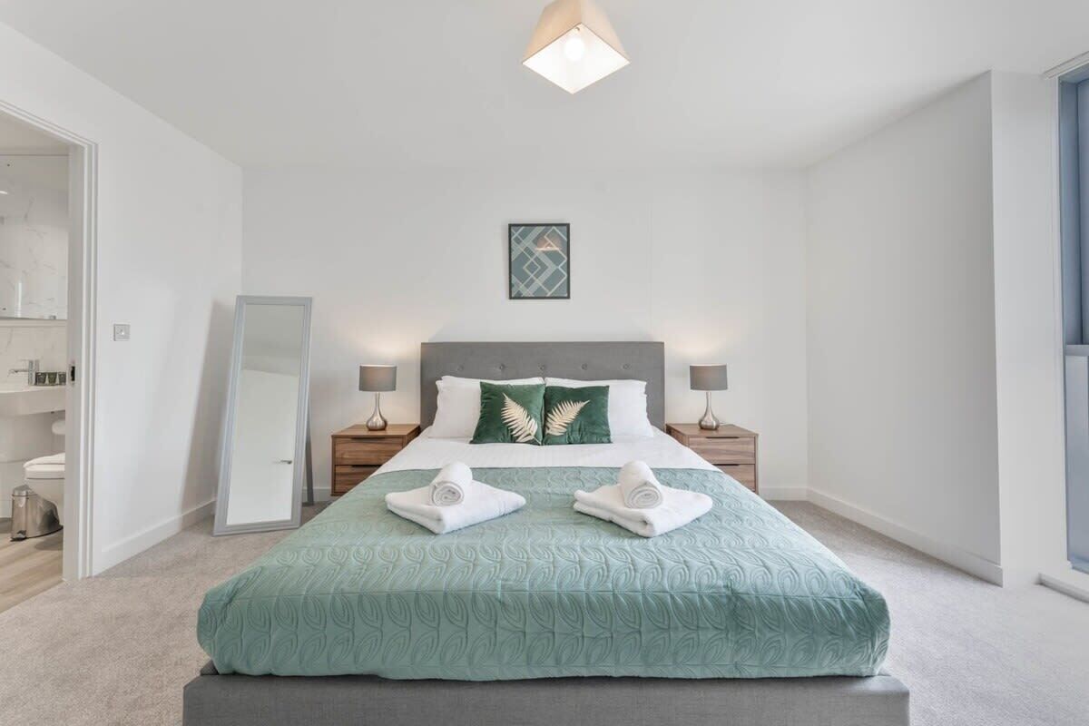 Quarto bem arrumado com cama, mesas de cabeceira, um espelho e um quadro na parede.