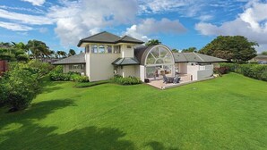 A modern house with a large glass conservatory, a well-maintained lawn, and a clear sky.