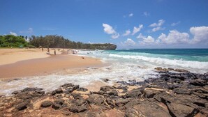 A beach with rocky foreground, clear skies, and people enjoying the water.