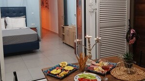 Ruokailutila, jossa on katettu ruokapöytä, viereisessä huoneessa sänky ja liukuovi, joka johtaa toiseen huoneeseen.