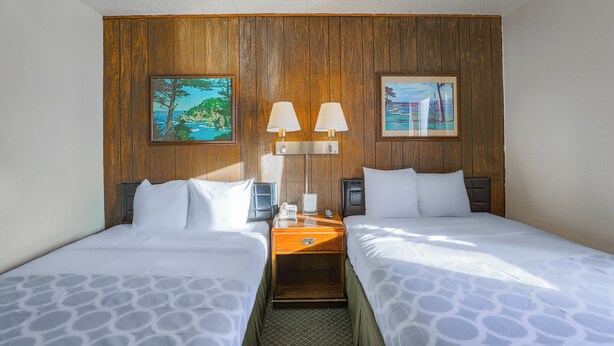 Een hotelkamer met twee bedden, houten lambrisering en twee schilderijen.