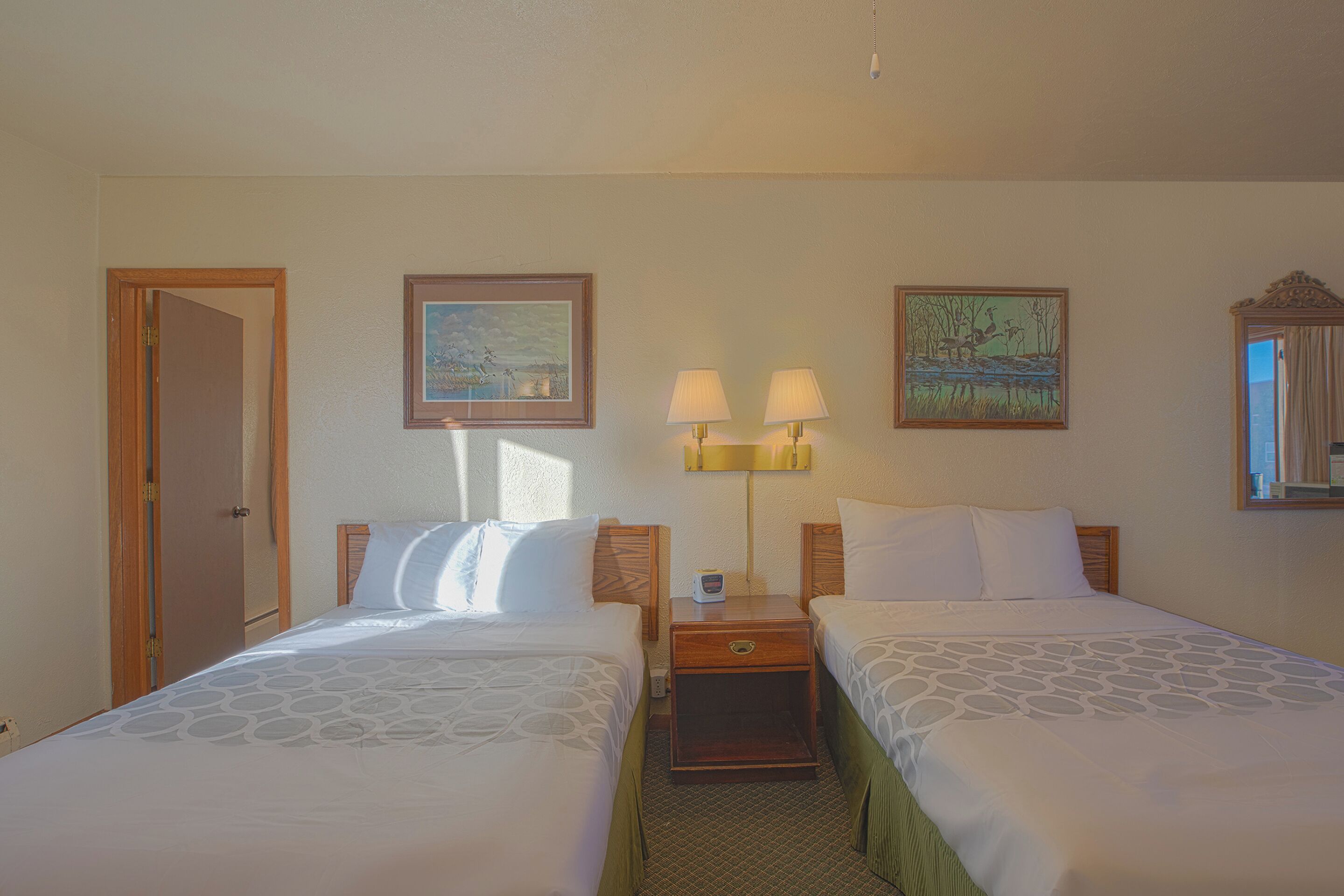 A hotel room with two beds, a nightstand with lamps, and two framed pictures on the wall.