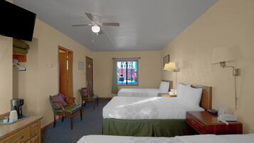 A hotel room with two beds, a desk, a chair, a television, a ceiling fan, and a window with a view of a building.