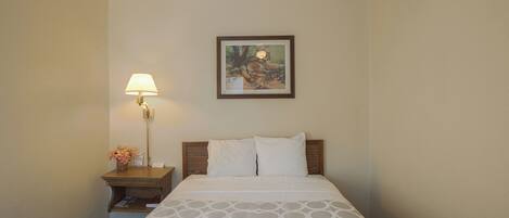 A hotel room with a bed, a nightstand with a lamp, and a framed picture on the wall.