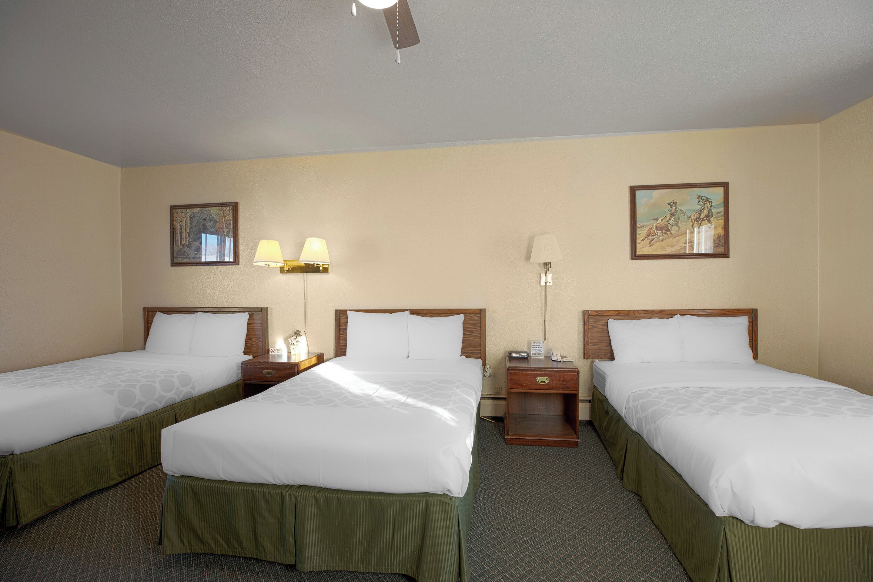 A hotel room with two single beds, a nightstand with a lamp, a small table, and a wall-mounted telephone.