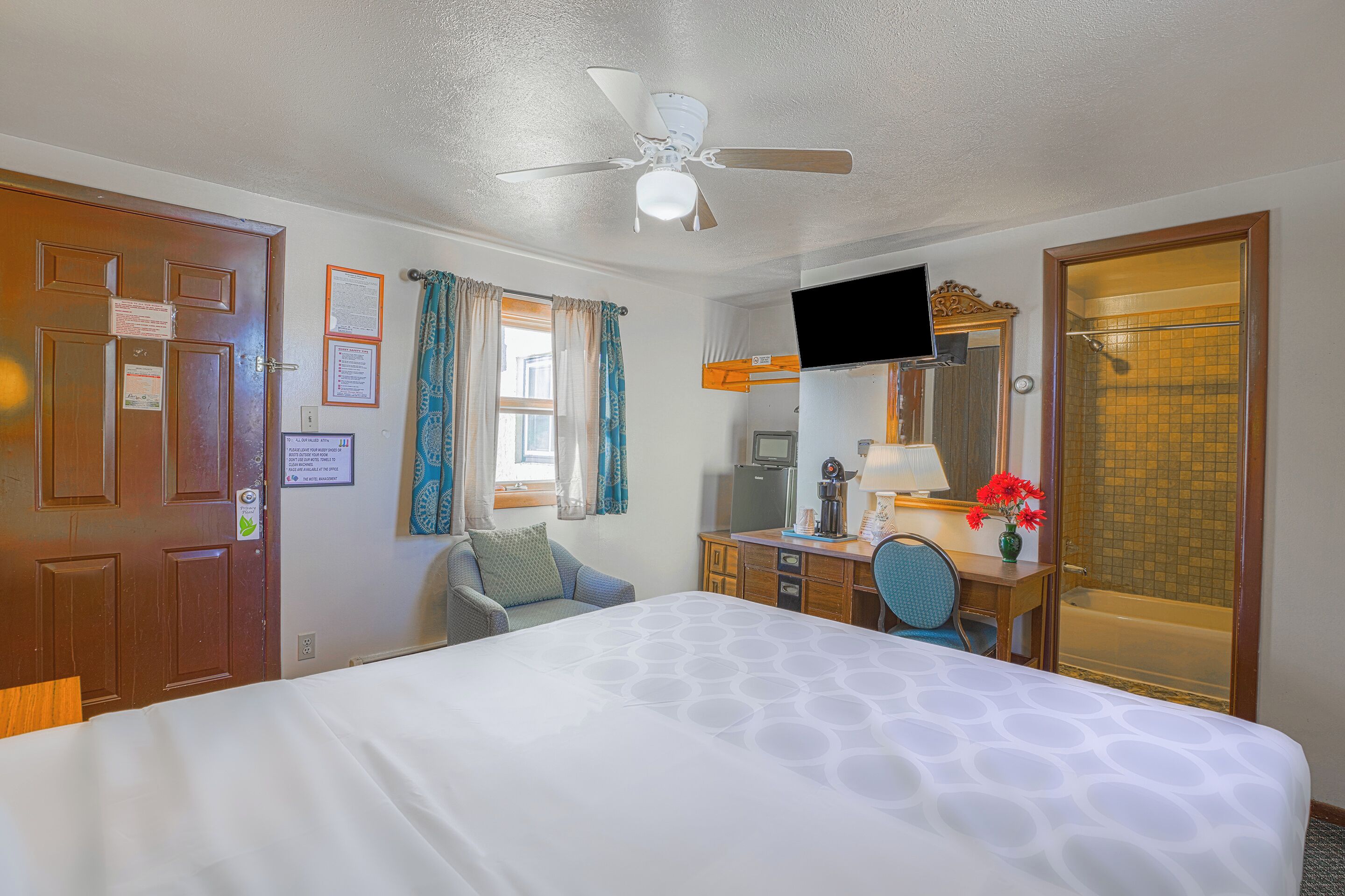 A hotel room with a bed, a desk, a chair, a television, and a shower.