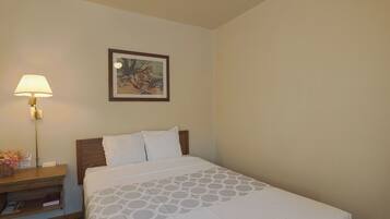 A hotel room with a neatly made bed, a bedside table with a lamp, a framed picture on the wall, and a small basket with flowers.