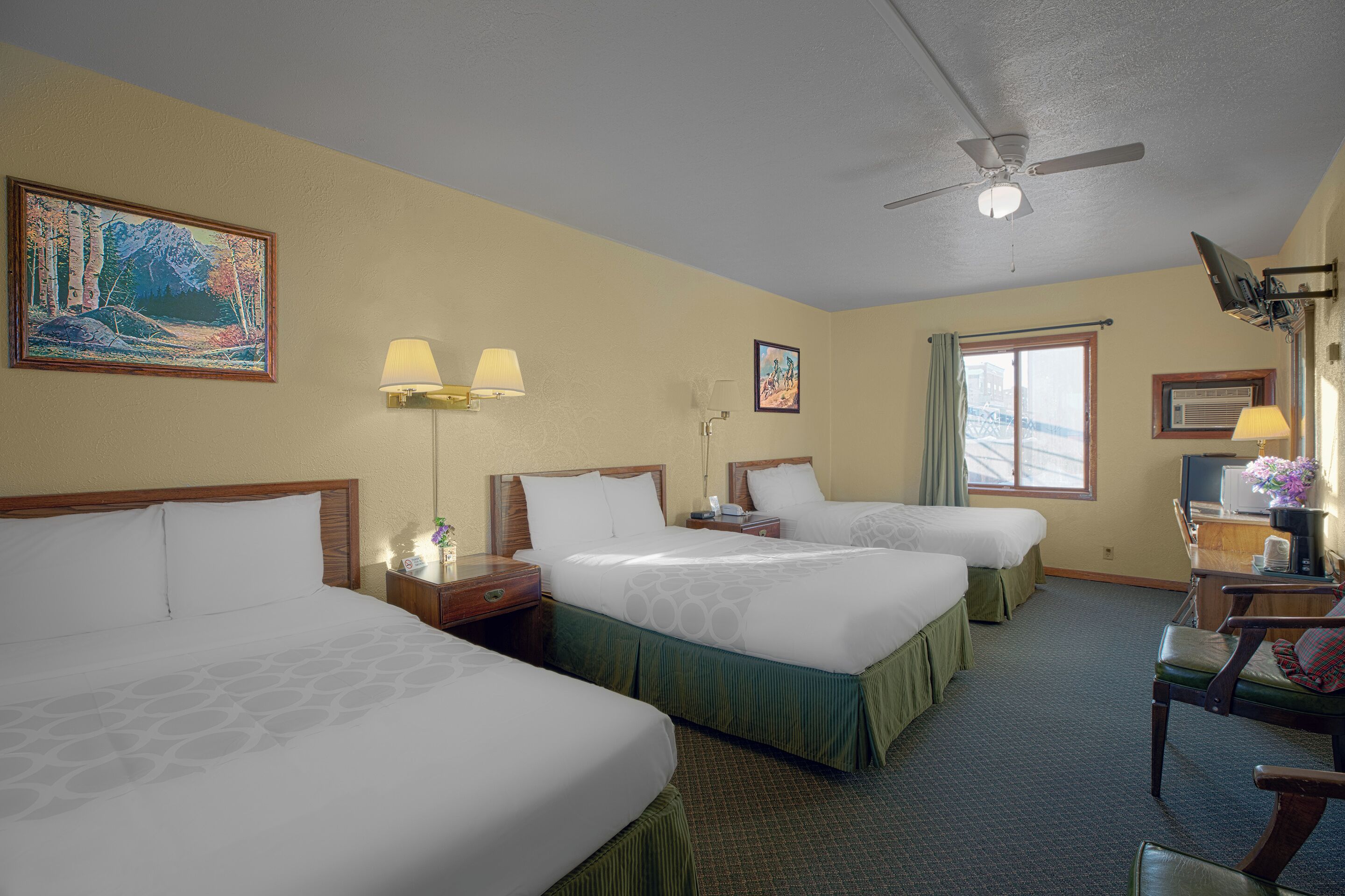 A hotel room with three beds, a ceiling fan, and a desk with a chair.