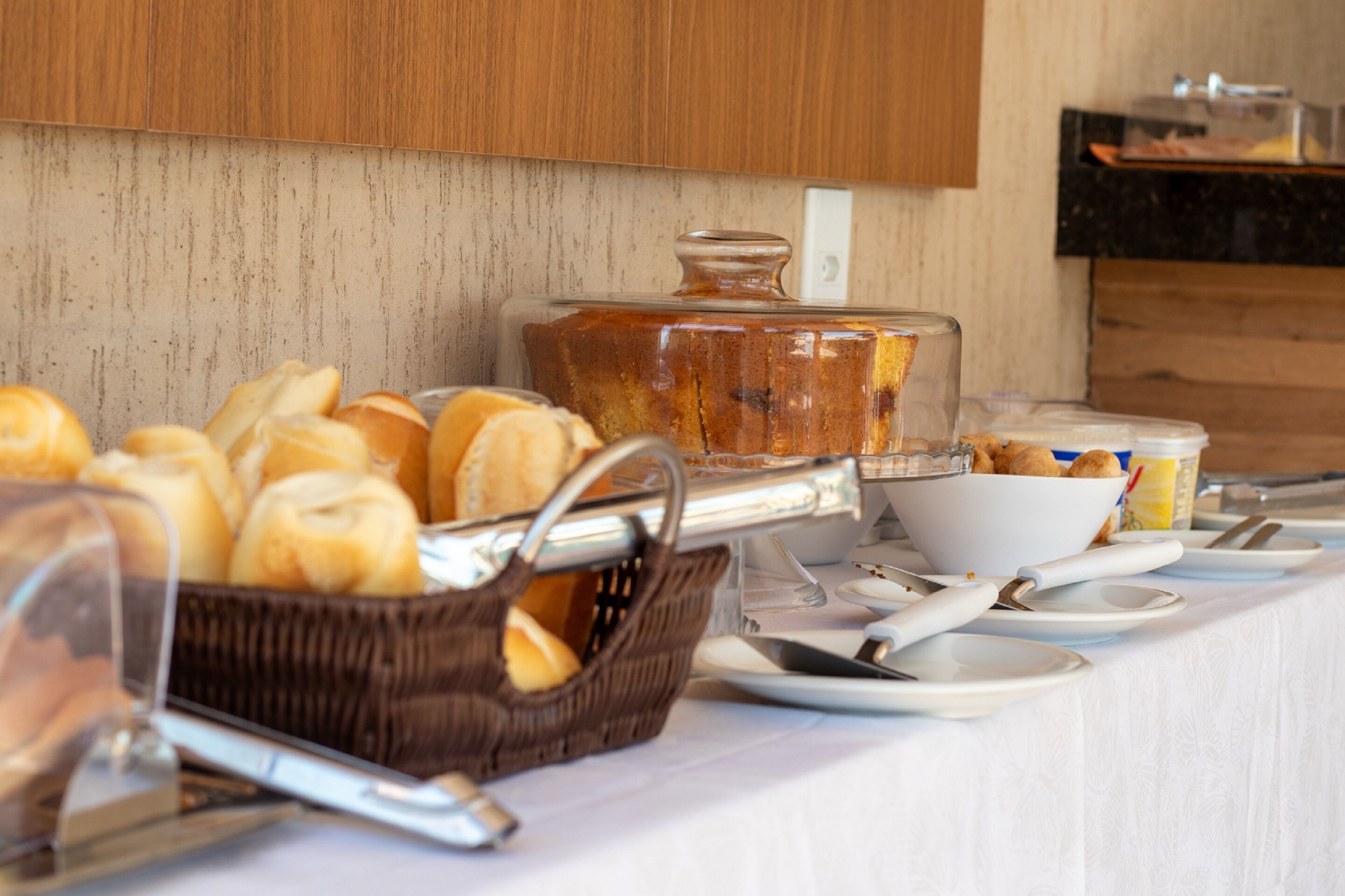 A buffet setup with bread, pastries, and a large container of food.