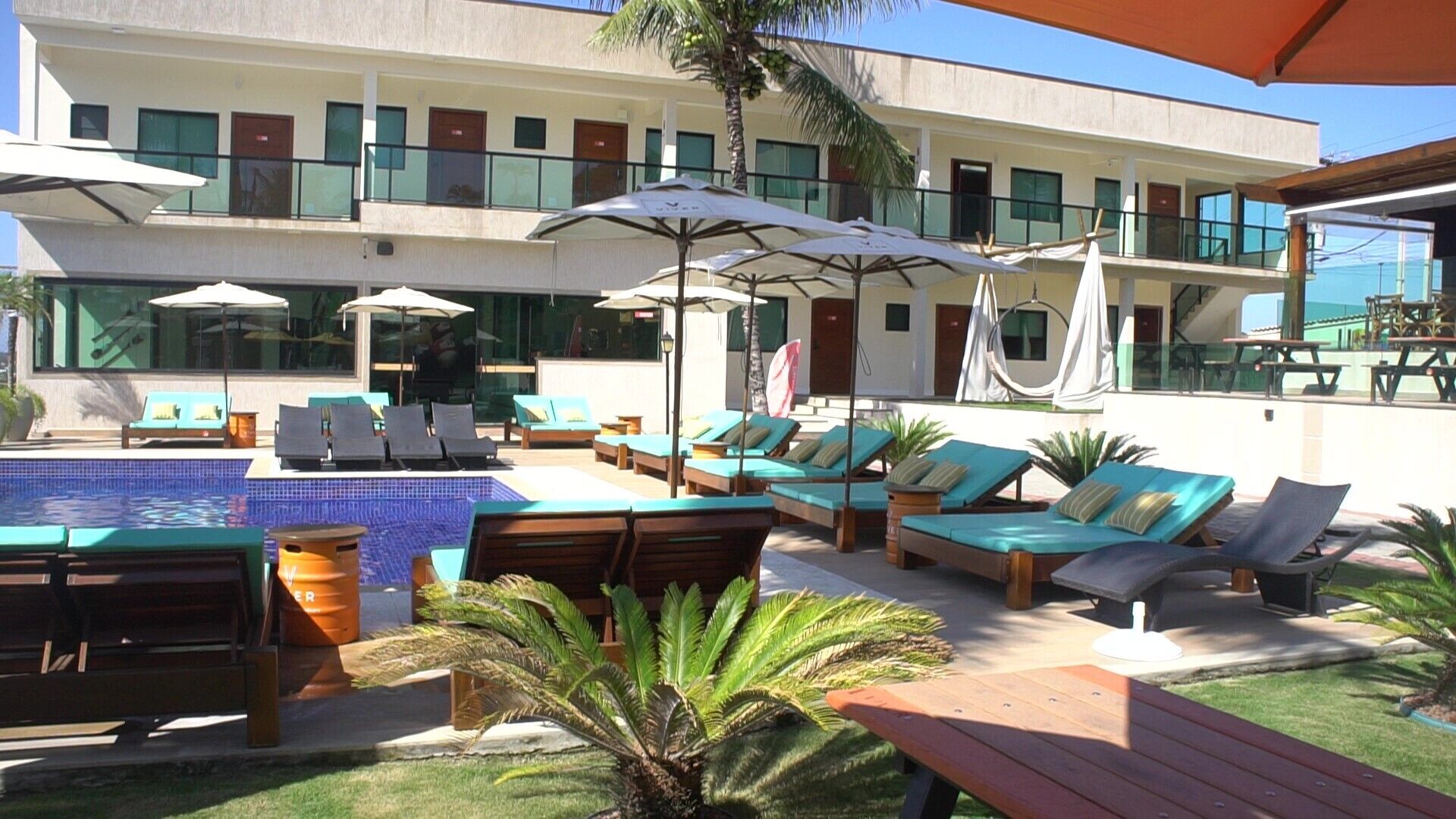 A pool area with sun loungers, umbrellas, and a building with multiple windows and balconies.