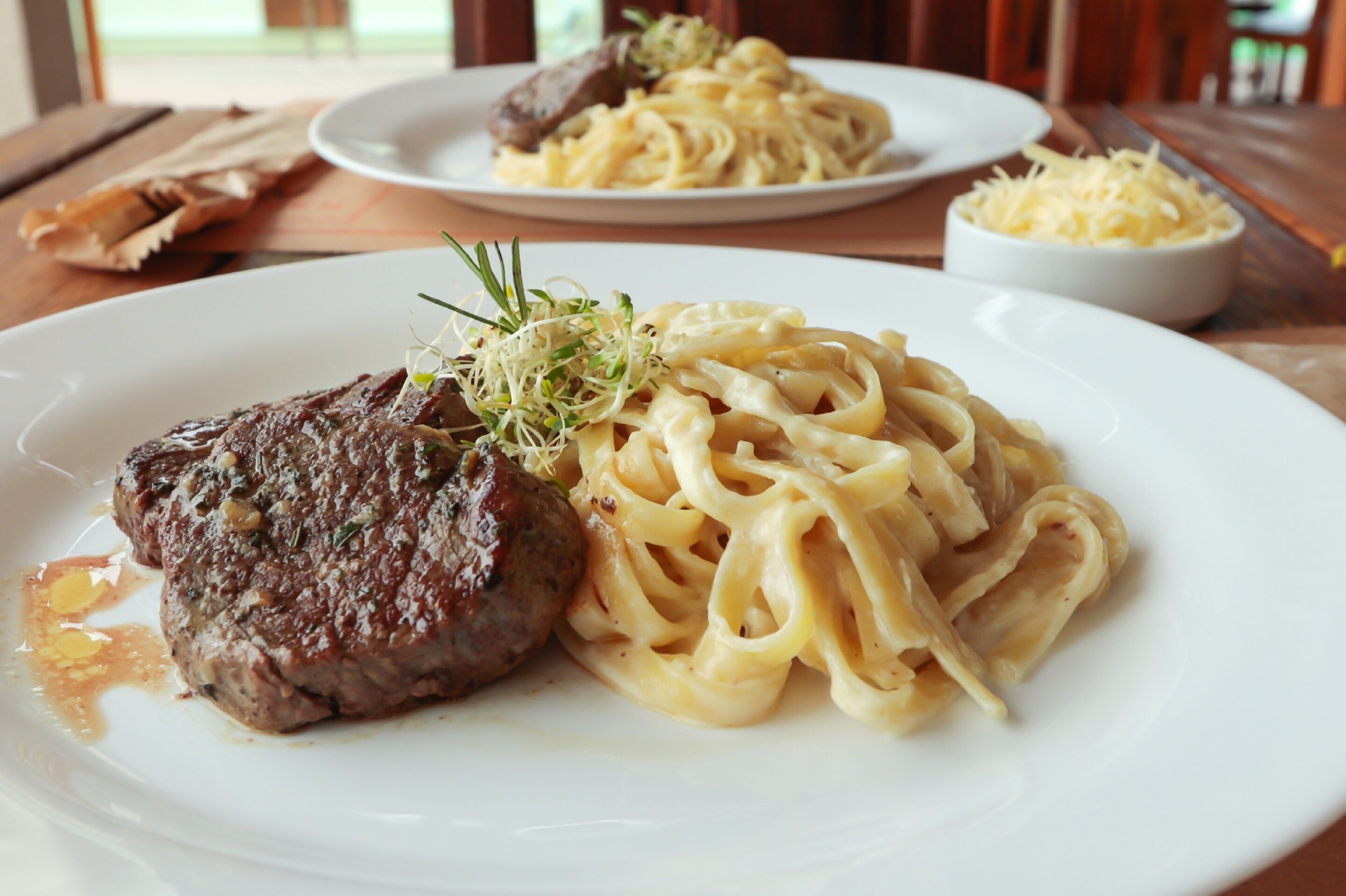 Une assiette de pâtes, accompagnée d’un steak et d’une garniture, est posée sur une table en bois.