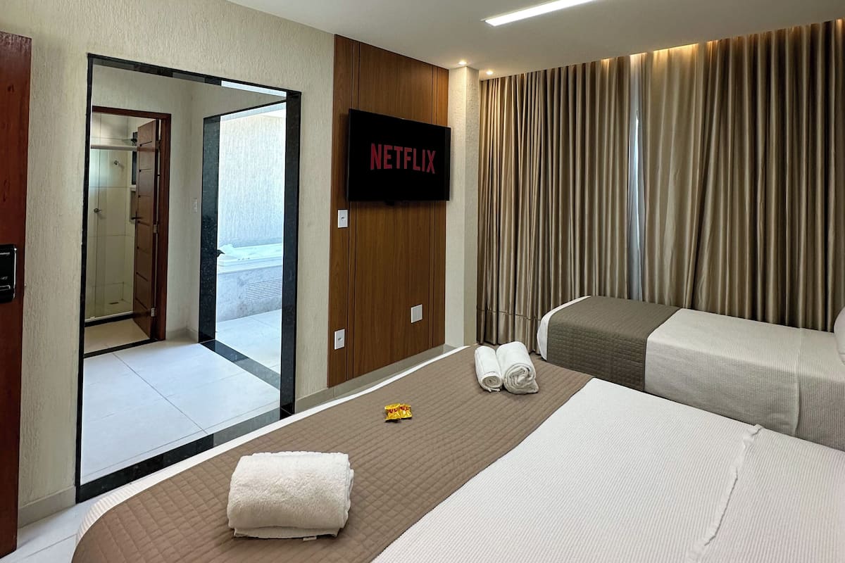 A hotel room with a bed, a TV mounted on the wall, a bathroom visible through an open door, and a view of the sea.