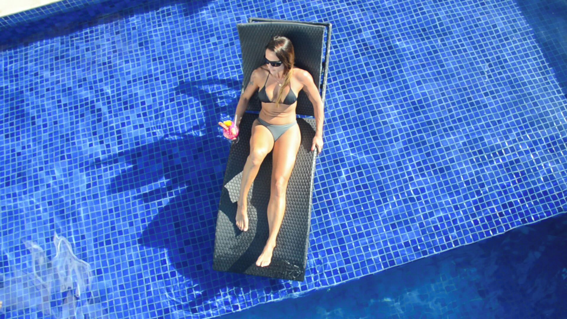 A person sunbathing on a lounge chair in a pool with blue mosaic tiles.
