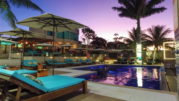 A pool area with lounge chairs and umbrellas, a pool with water features, and a building with a sign that reads "ER". -  Viver Pousada (Saquarema)