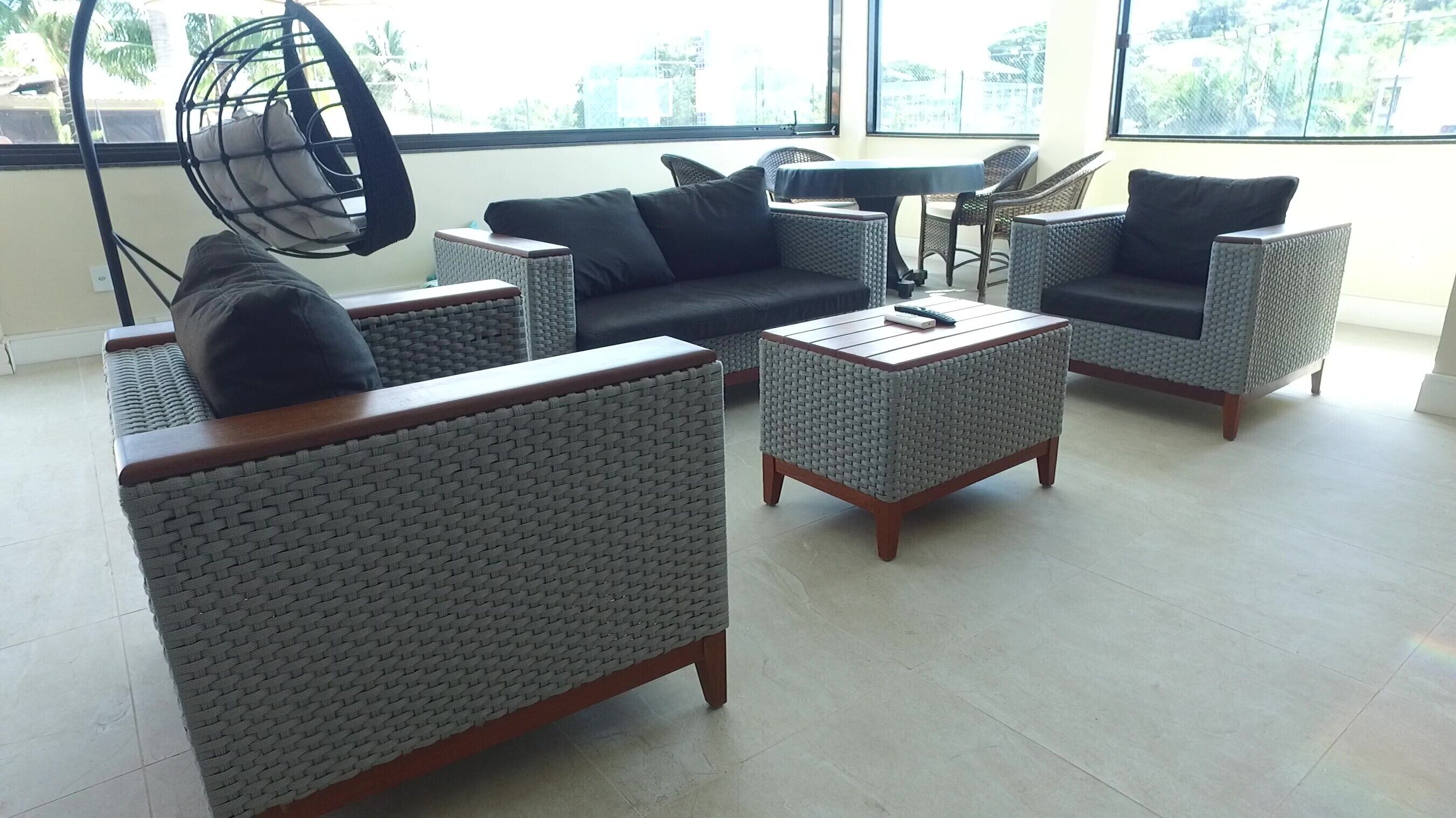 Una sala de estar moderna con muebles de mimbre, un sillón colgante y vistas de la ciudad a través de grandes ventanales.