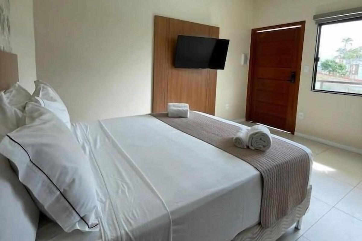 Quarto de hotel com cama, televisão na parede e janela.