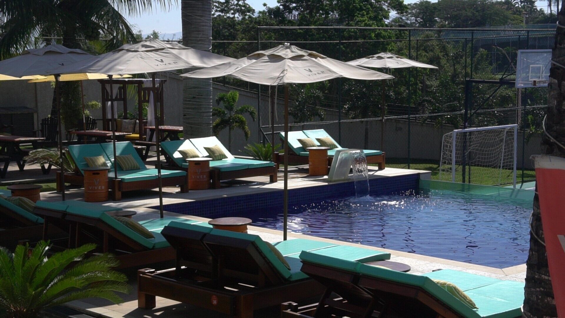 A pool area with lounge chairs, umbrellas, and a basketball hoop.