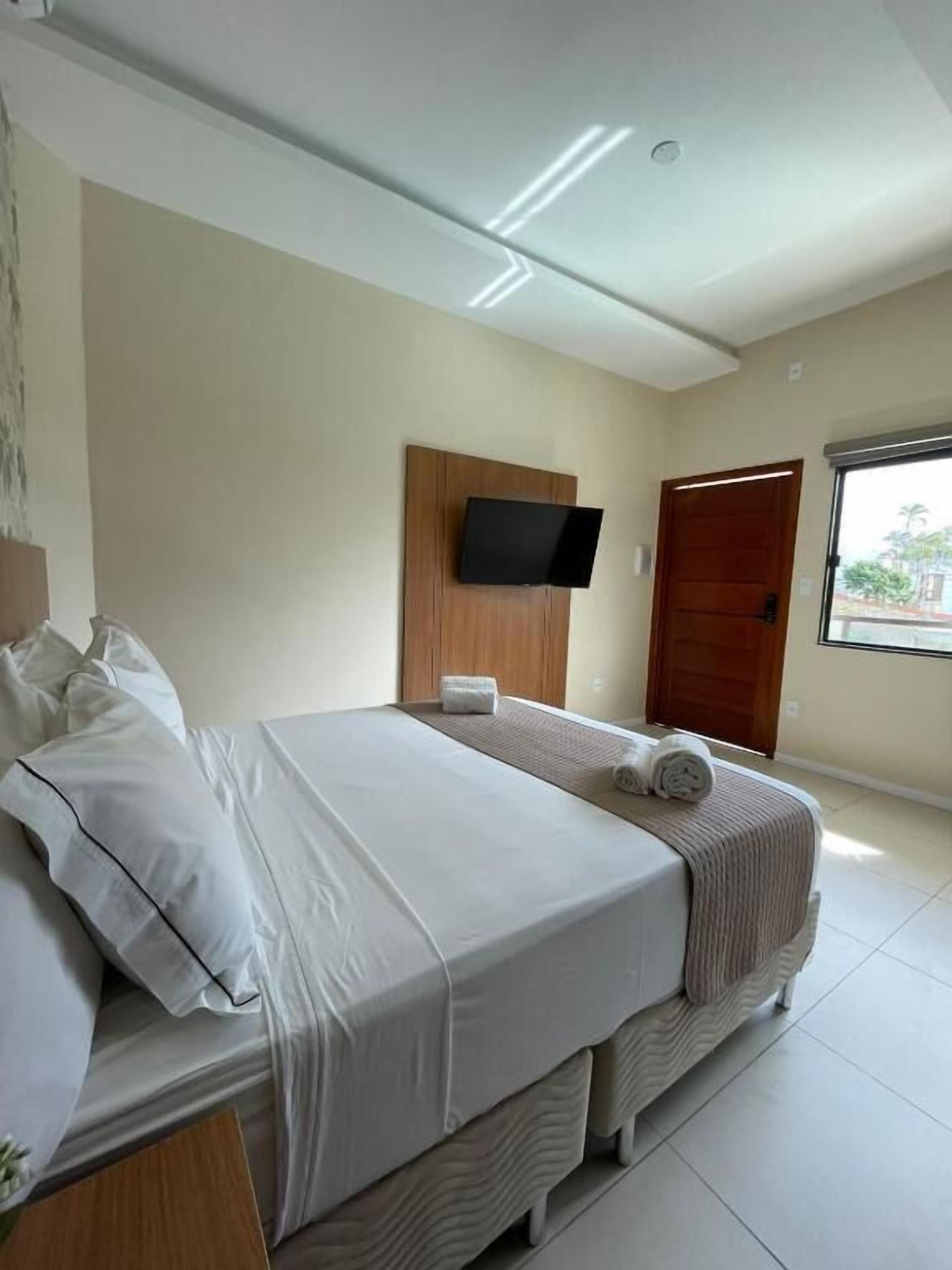 Une chambre d’hôtel avec un lit, un téléviseur fixé au mur, une porte en bois et une fenêtre.