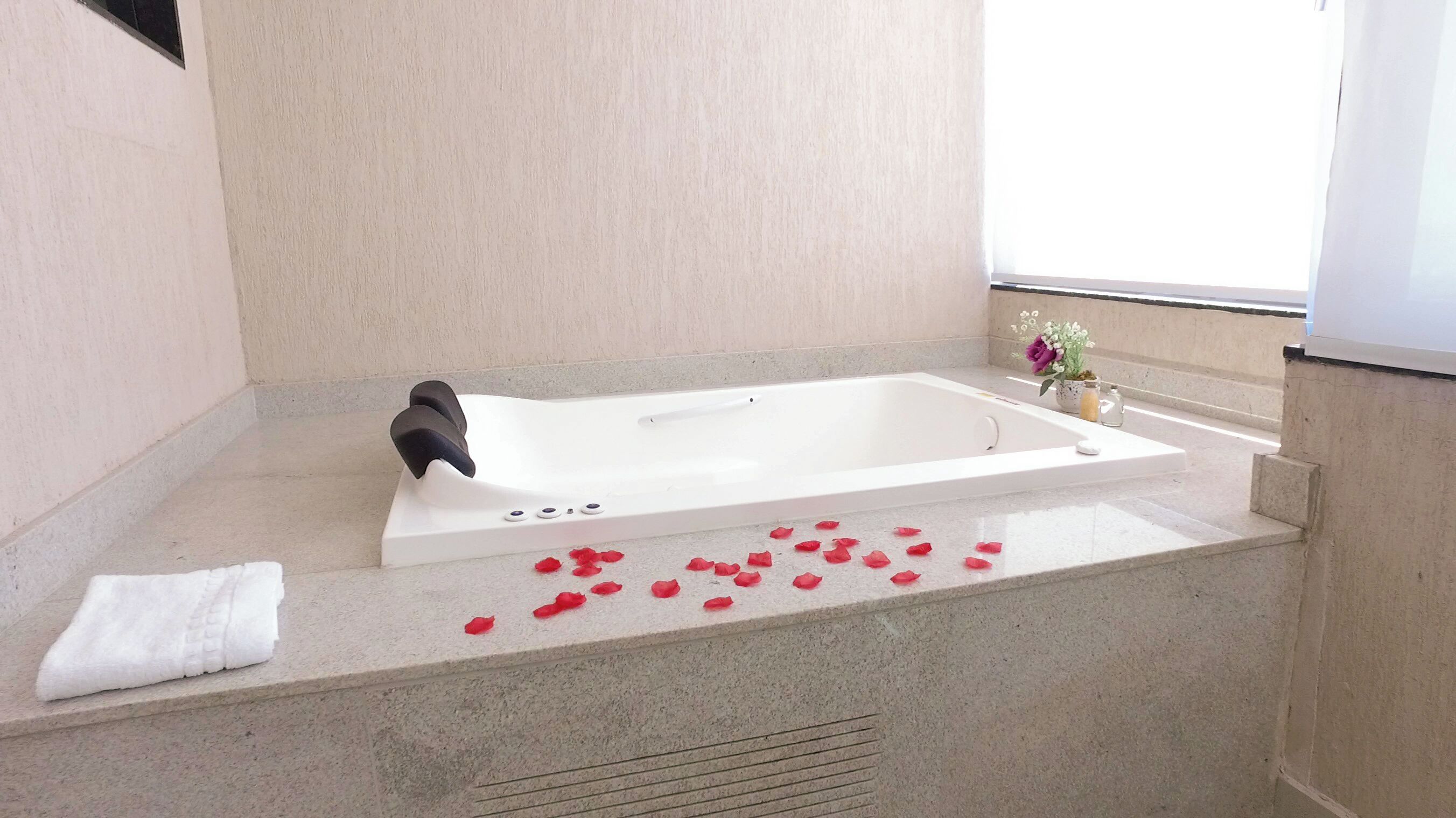 Une salle de bain avec une baignoire, une serviette et des pétales de rose sur le sol.