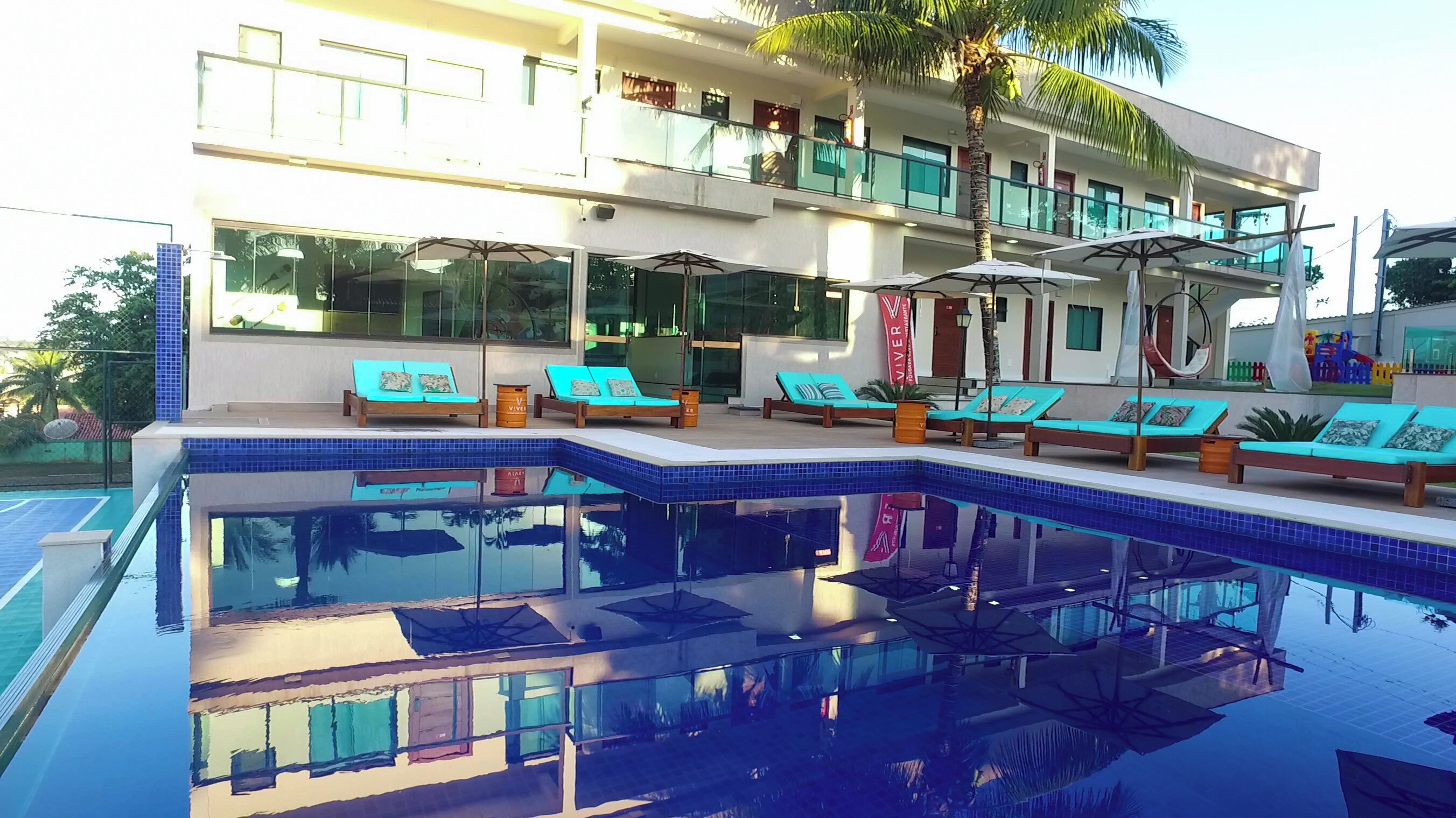 Um hotel moderno com piscina, várias áreas de estar com espreguiçadeiras e um edifício de dois andares com varandas.