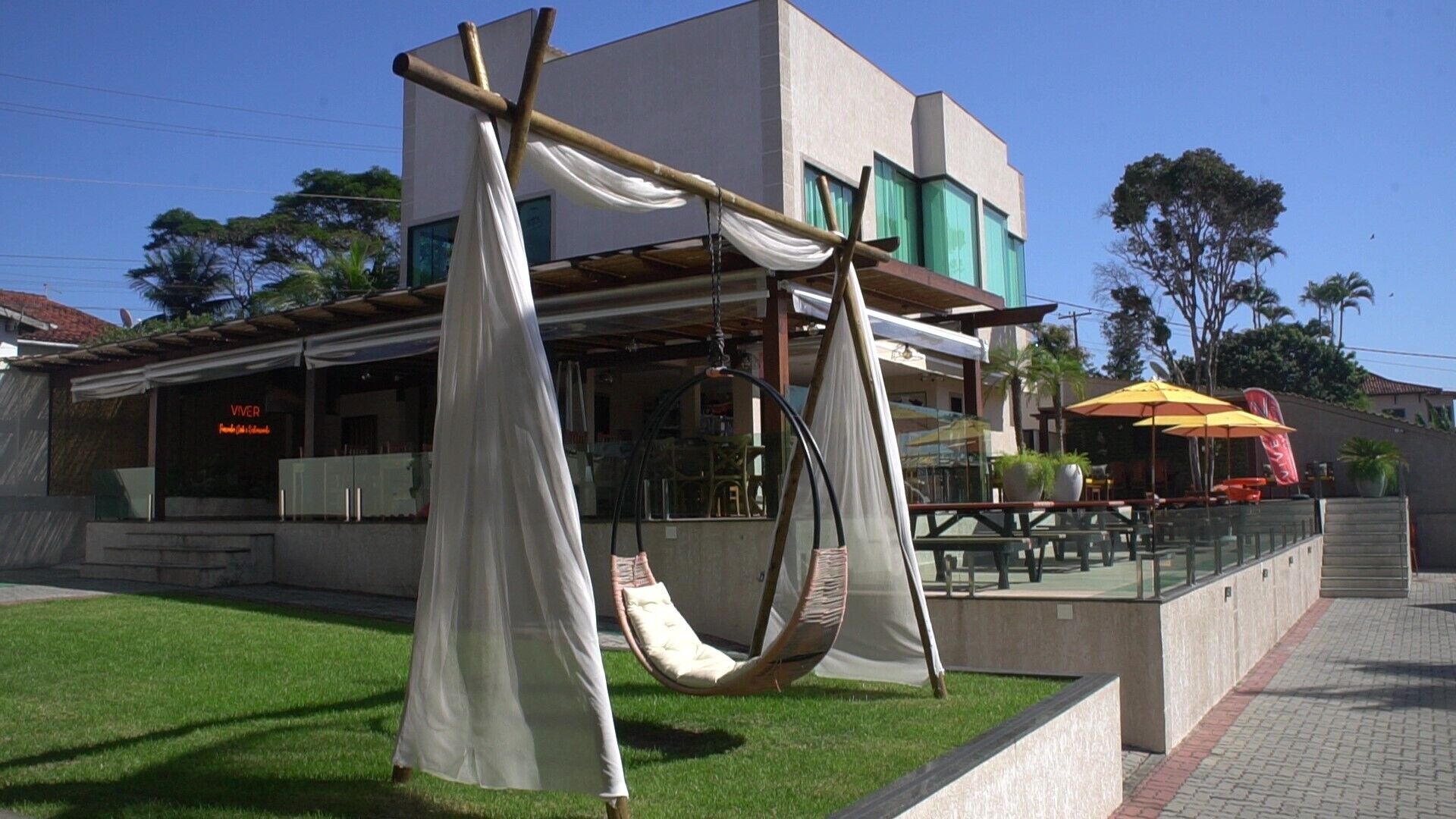 A building with a modern design, featuring a restaurant named 'Viver' and outdoor seating with a hammock chair.