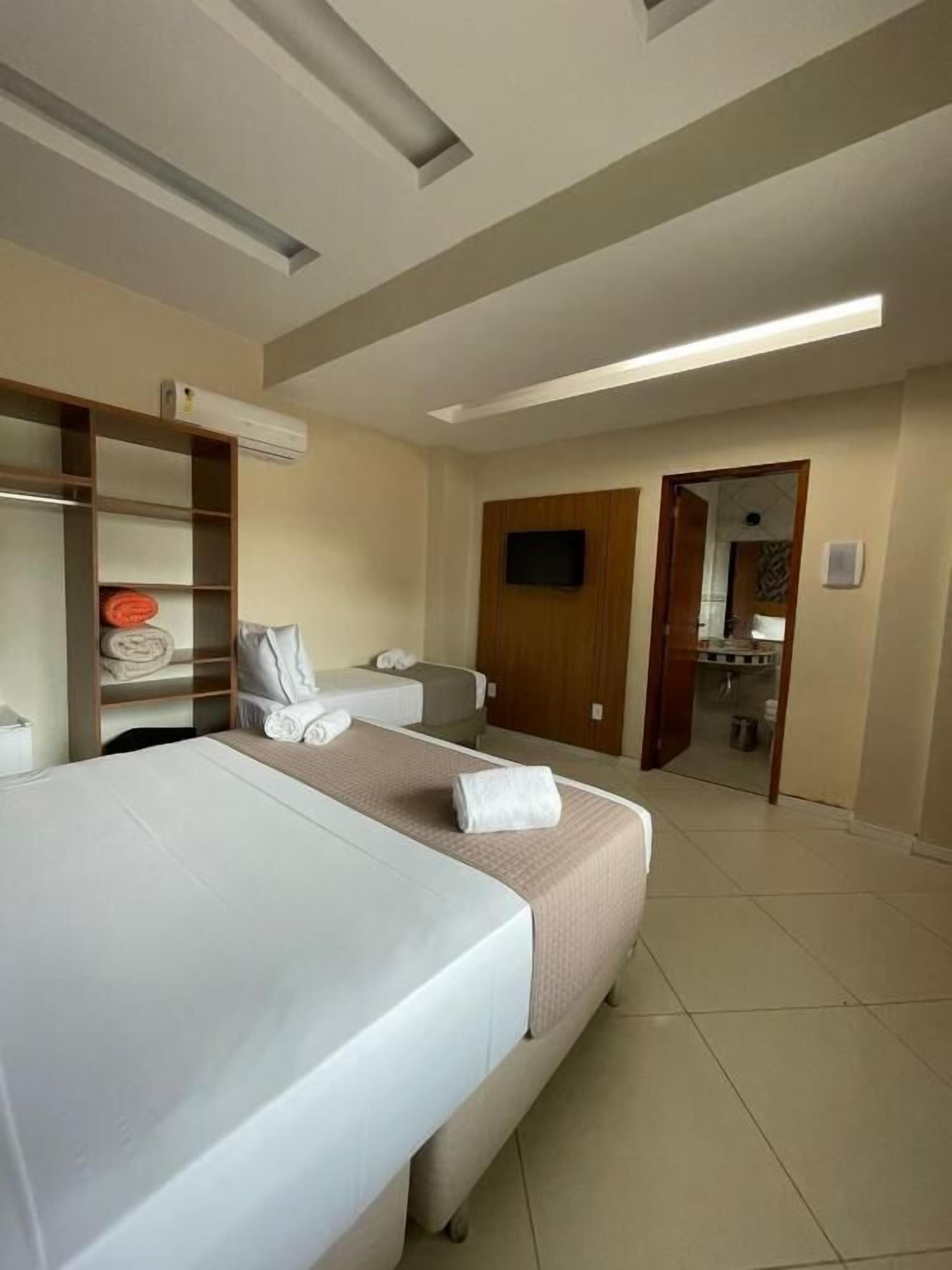 Camera d'albergo con due letti, un armadio, una televisione e un bagno visibile attraverso una porta aperta.